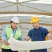 Male and female engineers discussing blueprints at a construction site, promoting teamwork and planning.