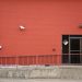 Urban red brick wall with security camera and entrance, featuring safety signage and railing.