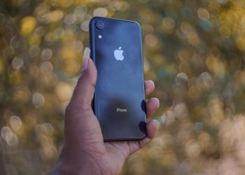 A close-up of a hand holding a smartphone with a blurred outdoor background.