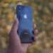 A close-up of a hand holding a smartphone with a blurred outdoor background.