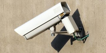 Close-up of a white security camera mounted on a beige wall in sunlight, emphasizing safety.