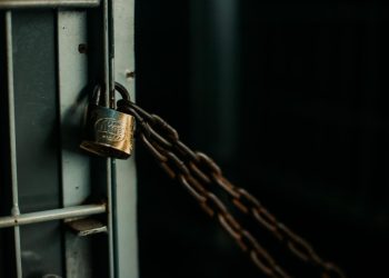 An artistic close-up photo of a faded padlock securing a chain on a metal door, symbolizing security.