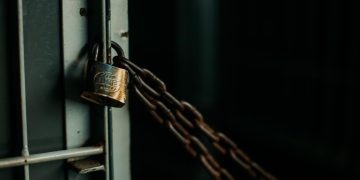 An artistic close-up photo of a faded padlock securing a chain on a metal door, symbolizing security.