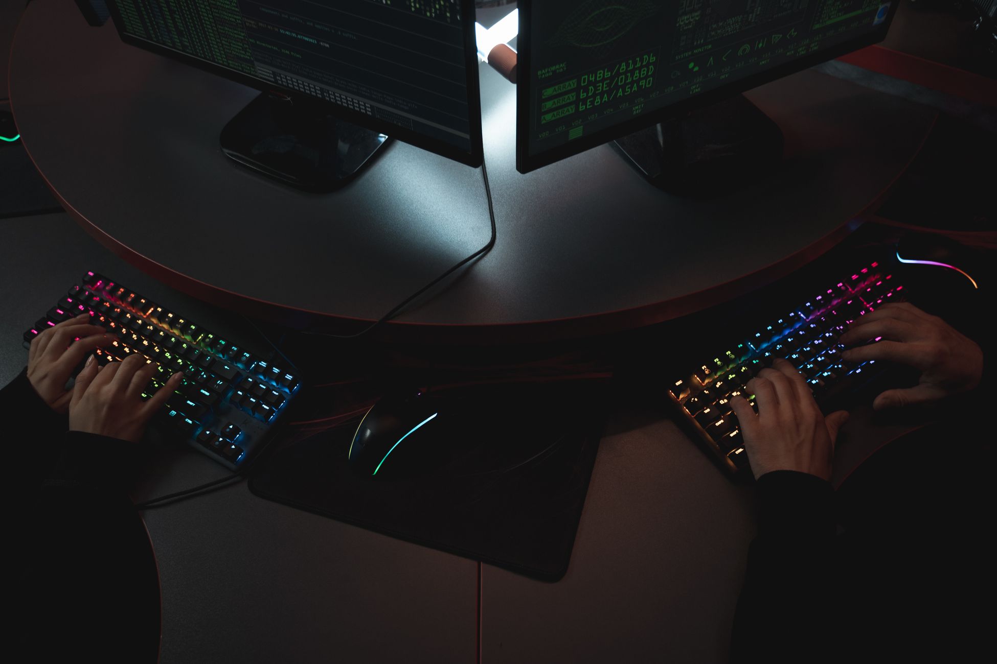 Two people typing on RGB keyboards with code on screens, indicating a cybersecurity environment.