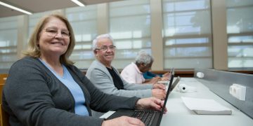 Smiling seniors learning computer skills in a modern classroom setting.
