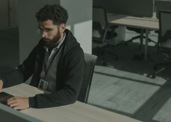 Bearded man working on a computer indoors, focused on cybersecurity tasks.