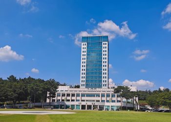 Tall office building under clear blue sky, surrounded by trees and grass lawn.