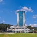 Tall office building under clear blue sky, surrounded by trees and grass lawn.