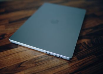 Closed laptop on a polished wooden table, emphasizing clean design and technology.