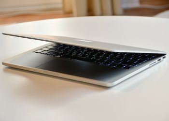 A modern MacBook laptop with a sleek design, slightly closed on a white table indoors.