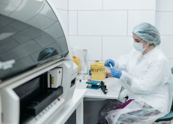 Scientist in protective gear examining samples in a medical lab setting, focusing on research.