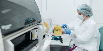 Scientist in protective gear examining samples in a medical lab setting, focusing on research.