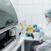 Scientist in protective gear examining samples in a medical lab setting, focusing on research.