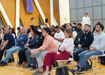 A diverse audience attentively listens during an indoor seminar, showcasing a collaborative learning environment.