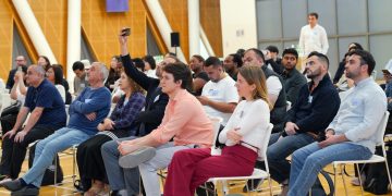A diverse audience attentively listens during an indoor seminar, showcasing a collaborative learning environment.