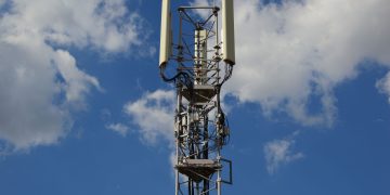 A tall cellular communication tower against a vivid blue sky, symbolizing modern technology.