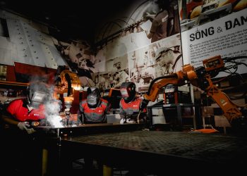 Three welders in protective gear working with robots in a high-tech industrial workshop.
