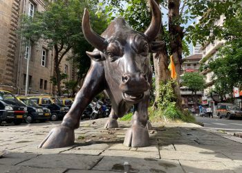 A prominent bull statue amidst a bustling urban street scene showcasing art and architecture.