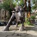 A prominent bull statue amidst a bustling urban street scene showcasing art and architecture.