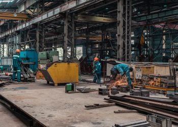 Workers in a metal workshop engaged in active construction and welding tasks.