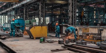 Workers in a metal workshop engaged in active construction and welding tasks.