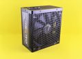 Black computer power supply unit with fan displayed against yellow background.