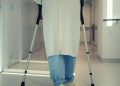A senior patient using crutches to walk down a hospital corridor, symbolizing recovery and mobility assistance.