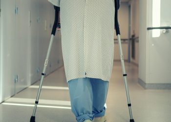 A senior patient using crutches to walk down a hospital corridor, symbolizing recovery and mobility assistance.