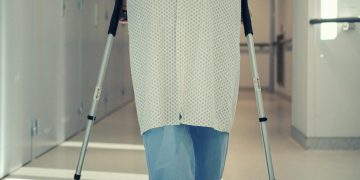 A senior patient using crutches to walk down a hospital corridor, symbolizing recovery and mobility assistance.