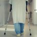 A senior patient using crutches to walk down a hospital corridor, symbolizing recovery and mobility assistance.