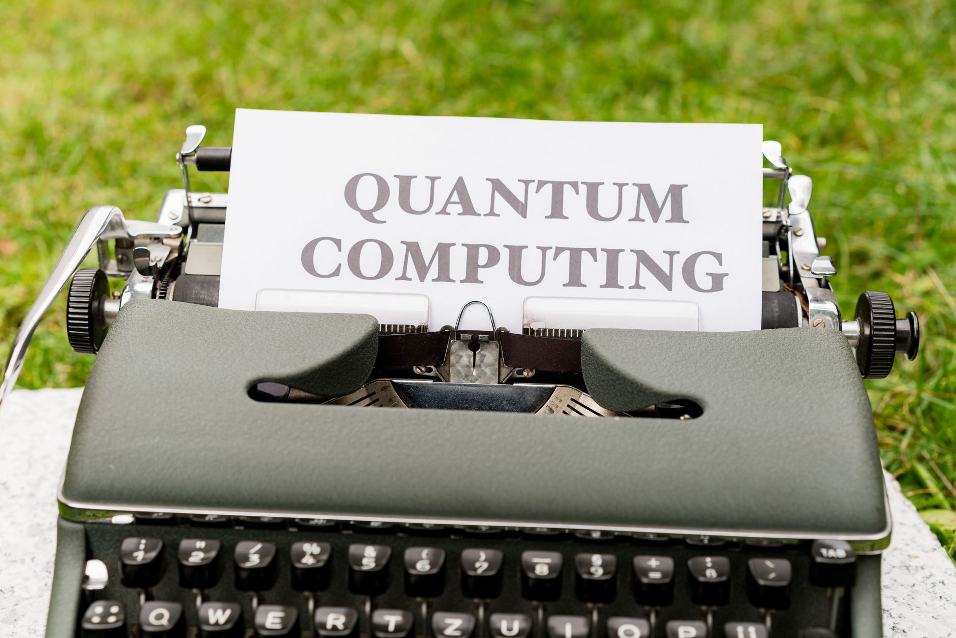 A typewriter with 'Quantum Computing' text outdoors on grass, blending old and new technologies.