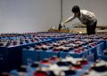 A worker checking many industrial batteries inside a facility. Indoor, industrial setting.