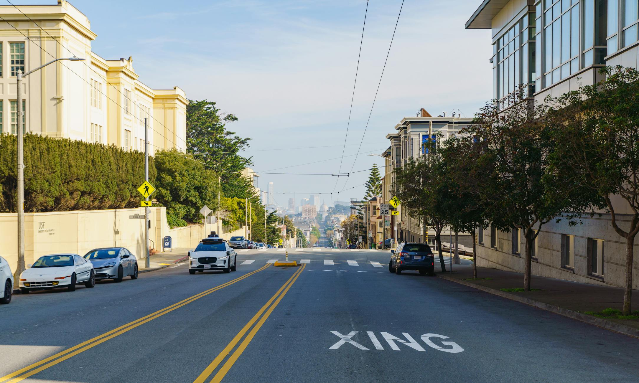 Street view of an urban neighborhood with distant city skyline under clear skies.
