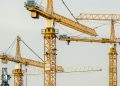 Cluster of yellow tower cranes at a construction site with a gloomy sky background.
