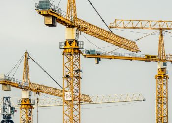 Cluster of yellow tower cranes at a construction site with a gloomy sky background.