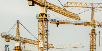 Cluster of yellow tower cranes at a construction site with a gloomy sky background.
