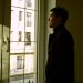 Contemplative man standing by a window indoors, gazing outside.