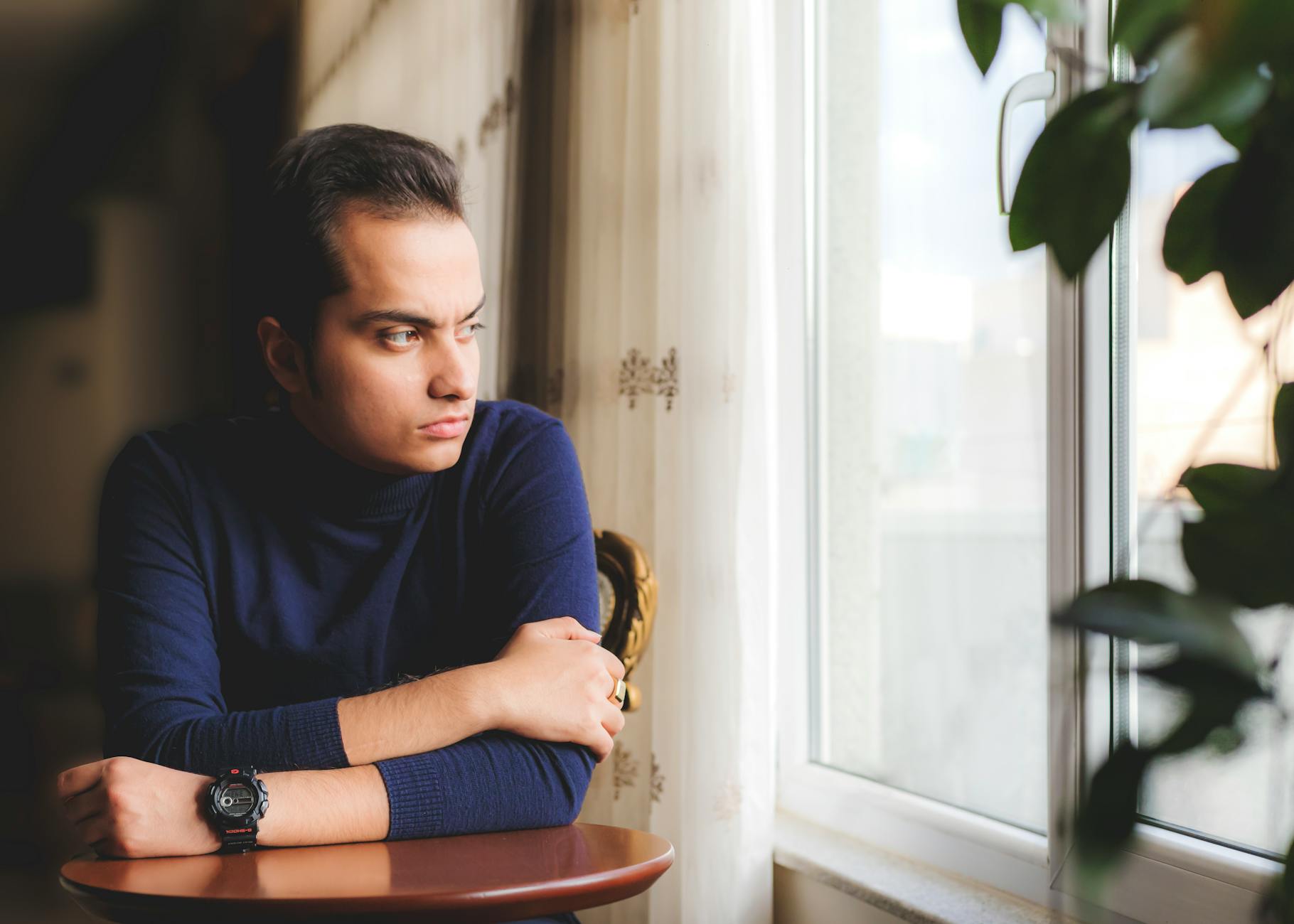 A man leans on a table, gazing thoughtfully out a window in Tabriz, Iran.