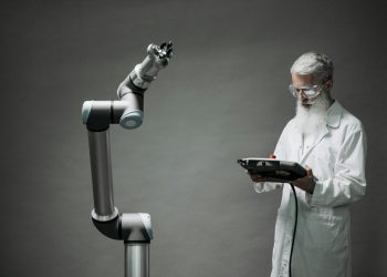 A scientist in a lab coat operates a high-tech robotic arm in a laboratory setting.
