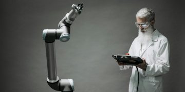 A scientist in a lab coat operates a high-tech robotic arm in a laboratory setting.