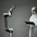 A scientist in a lab coat operates a high-tech robotic arm in a laboratory setting.