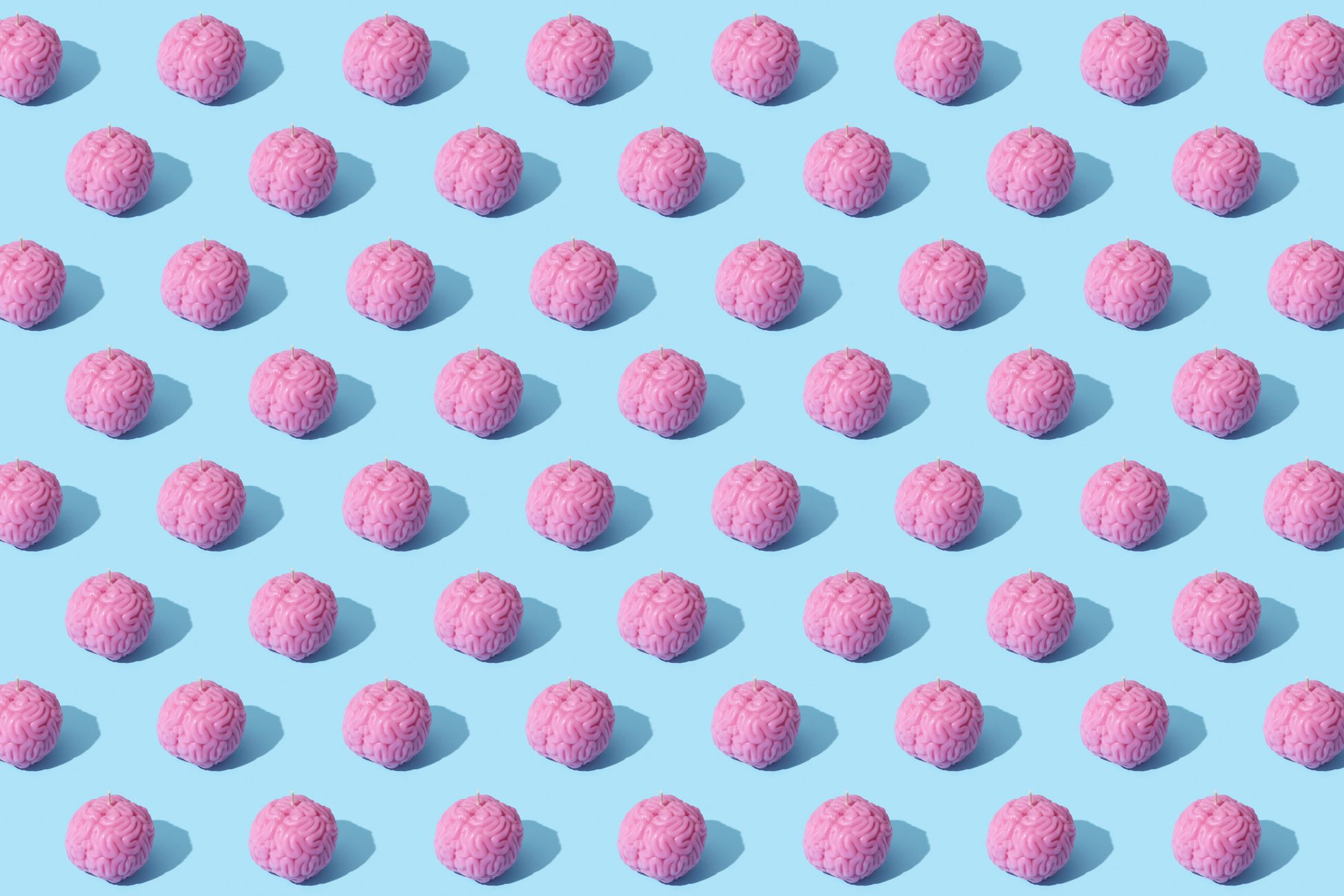Creative composition of pink brain models in a repeating pattern on a light blue surface, showcasing abstract thinking.