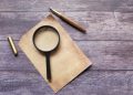 Vintage quill pen with magnifying glass on rustic wooden surface. Perfect for retro-themed designs.