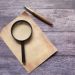 Vintage quill pen with magnifying glass on rustic wooden surface. Perfect for retro-themed designs.