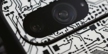 Macro shot of an electronic circuit design around a smartphone camera lens, showing intricate details.