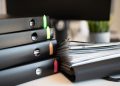 Stack of colorful ring binders and documents on a modern office desk setting.