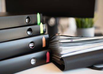 Stack of colorful ring binders and documents on a modern office desk setting.