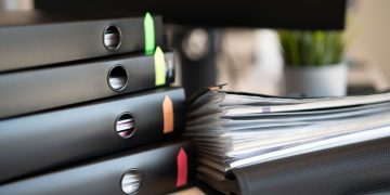 Stack of colorful ring binders and documents on a modern office desk setting.