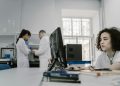 Focused woman working on a computer in a busy laboratory setting, showcasing teamwork and scientific research.