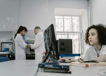 Focused woman working on a computer in a busy laboratory setting, showcasing teamwork and scientific research.